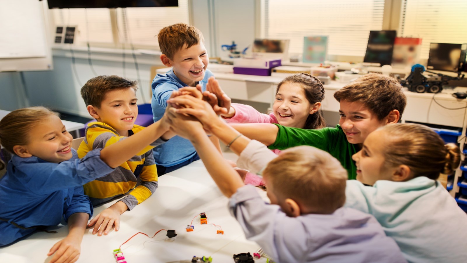 Børn ved et bord, der stabler deres hænder oven på hinanden som ved et kampråb