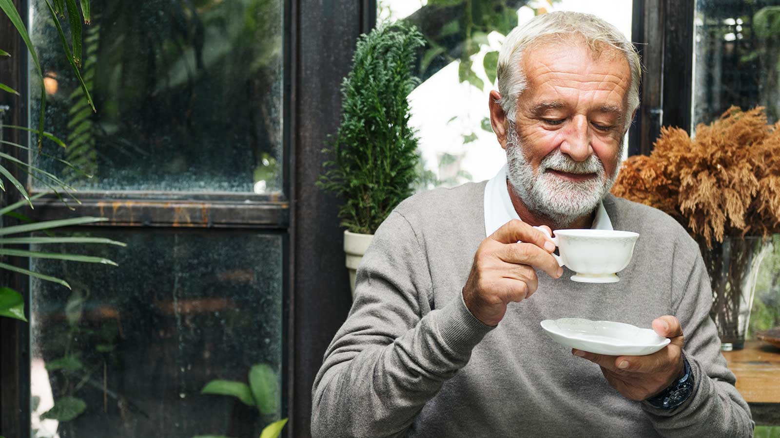 Ældre mand drikker kaffe i drivhus