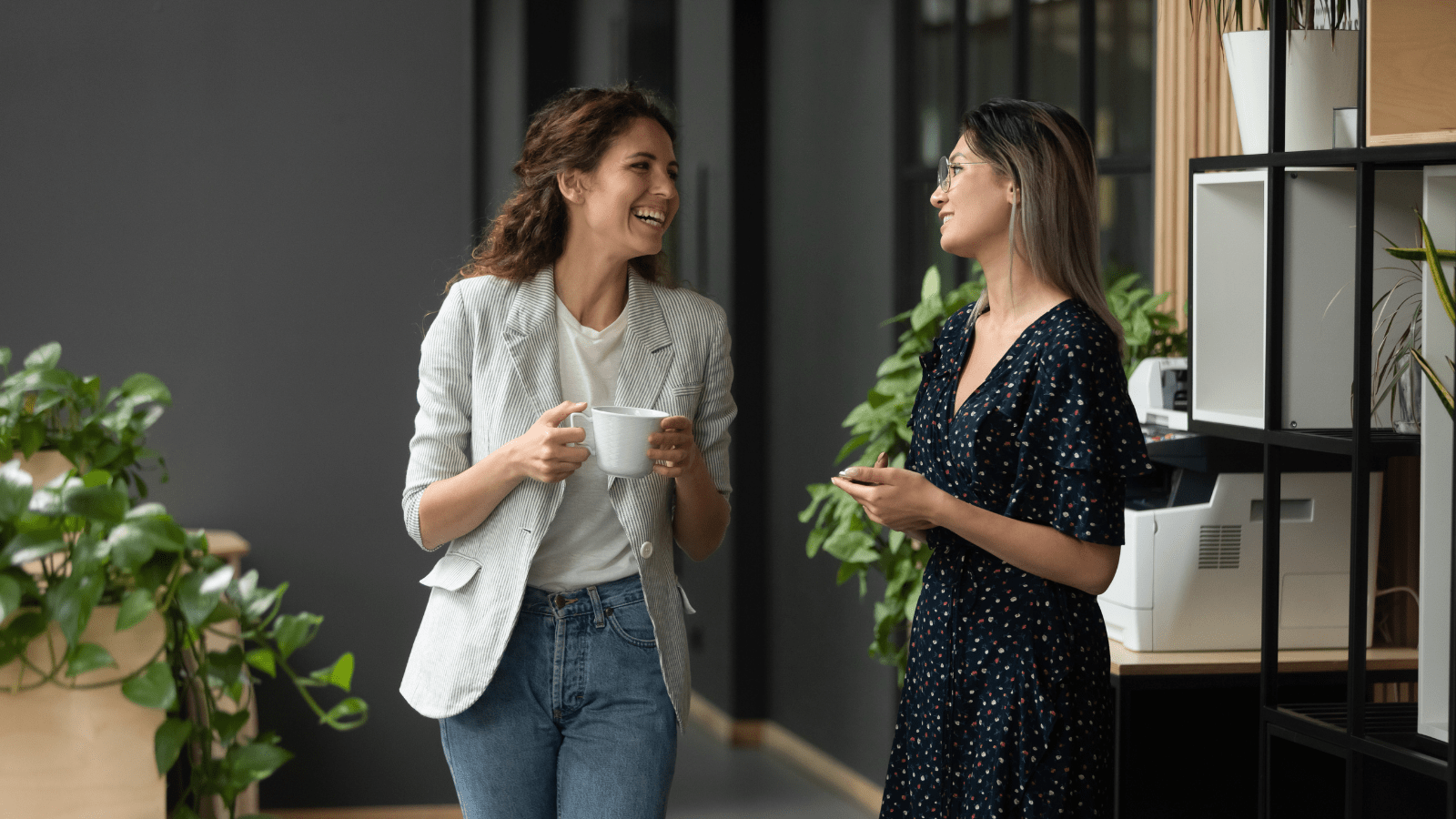 Kvinde med kaffekop smiler til kvindelig kollega